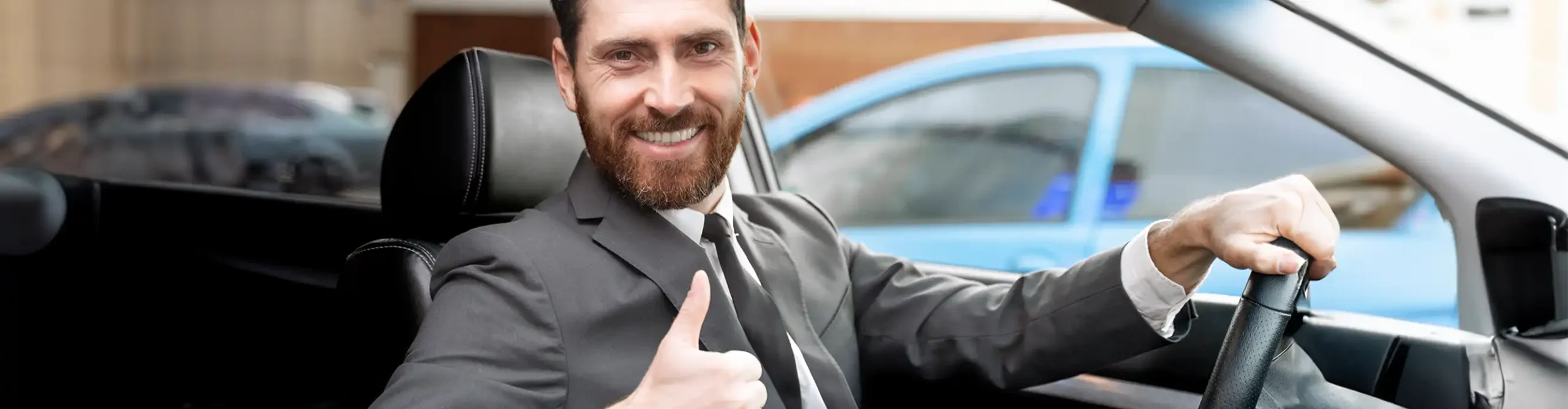 A smiling chauffeur in Dubai gives a thumbs-up while sitting in the driver's seat of a car.