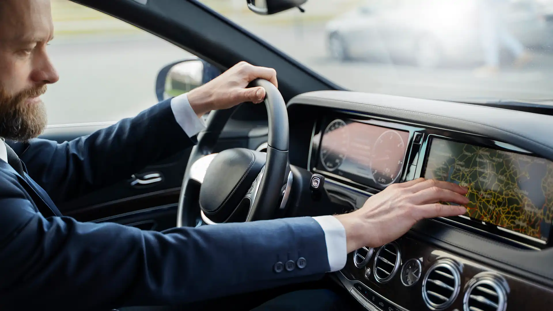 A man in a suit driving a car, interacting with the touch screen navigation system displaying a city map, suggesting a city tour drive.