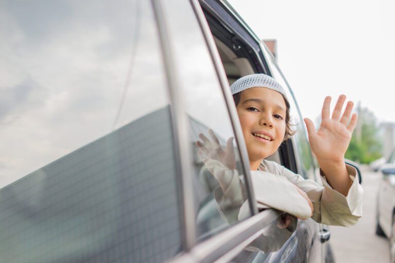 A happy boy waves from a car window, symbolizing safe and reliable school pick-up and drop-off services in Dubai.