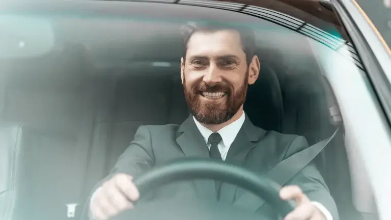 Man in a suit smiling while driving, representing a safe driver in Dubai.