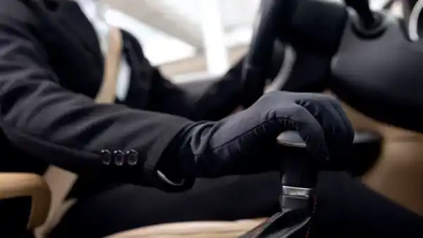 A professional corporate driver in Dubai, wearing a suit, holds the steering wheel while driving a luxury vehicle.