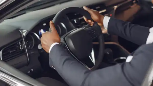 A professional driver providing Corporate Driver Service in Dubai, wearing a suit, holds the steering wheel while driving a luxury vehicle.