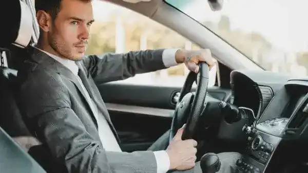 A serious-looking chauffeur in a gray suit, focused on driving a car, with a clean, modern interior. Hire a Safe driver services in Dubai.